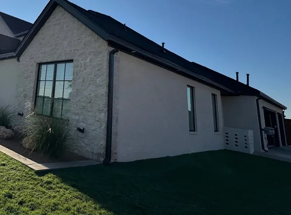 Dark seamless gutters along a white stone home under a clear blue sky