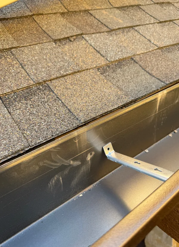 Inside a gutter along a shingle roof, a hidden hanger holding it to the board behind