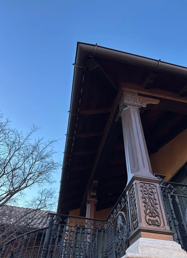 Looking up at a porch eave and its wood in full sun, a carved column below