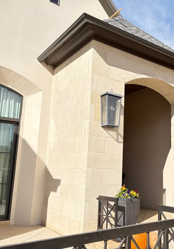 The gable over a limestone home's arched entry: dark gutters on the fascia and the soffit under the overhang