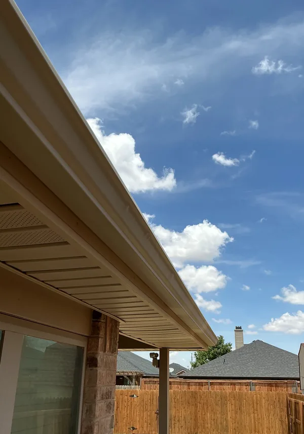 Looking up along a roof edge from below: the soffit under the overhang and the fascia with its gutter, against a sky with clouds