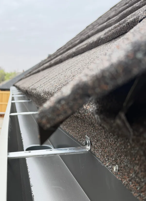 Looking along a new seamless gutter run and its hidden hangers, at the edge of a shingle roof.