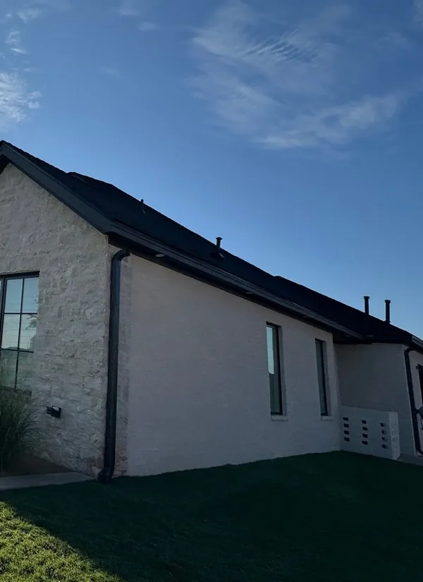 New dark gutters along a limestone and stucco home over a green lawn.