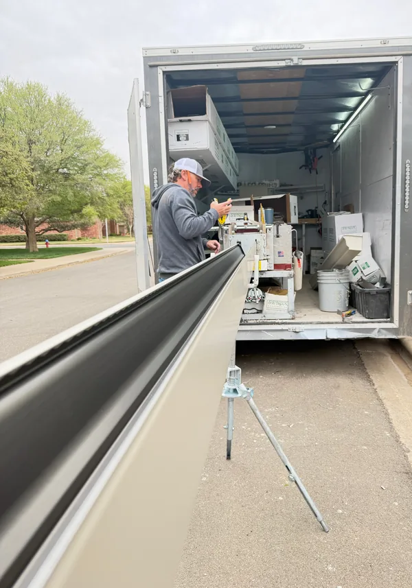 A Premier crew member at the gutter machine in an open trailer at the curb, a long new gutter coming out of it
