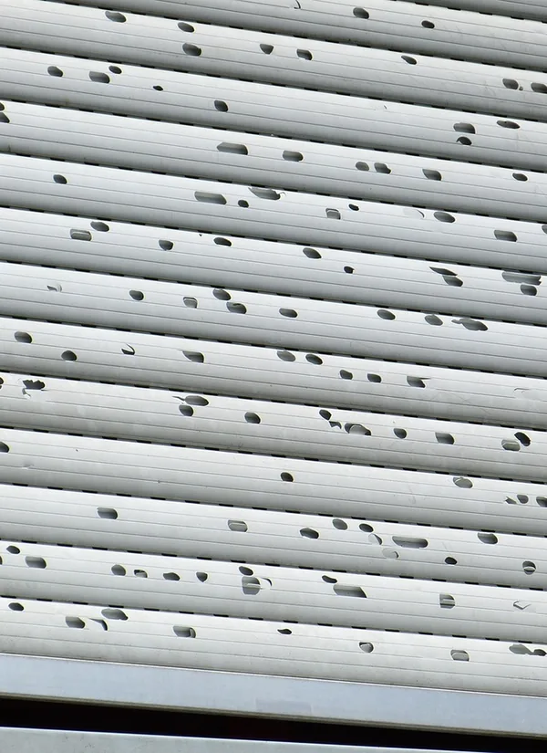 White metal shutter slats pocked with dents and holes from hail.