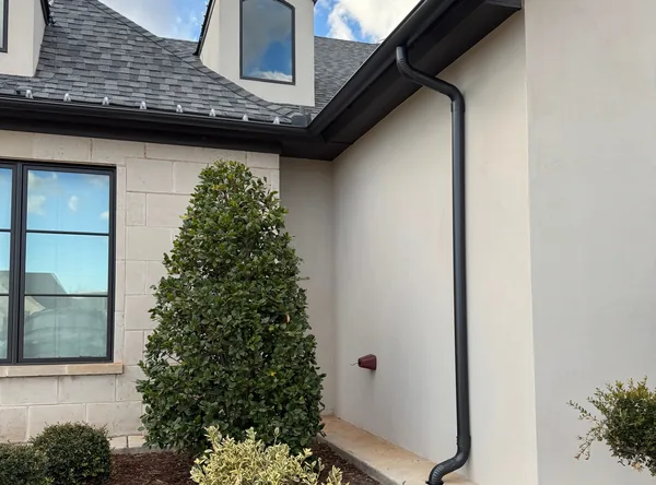 A black gutter and downspout on a white stucco home under a dormer