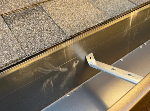Inside a new seamless gutter along a shingle roof, with its hidden hanger across the trough
