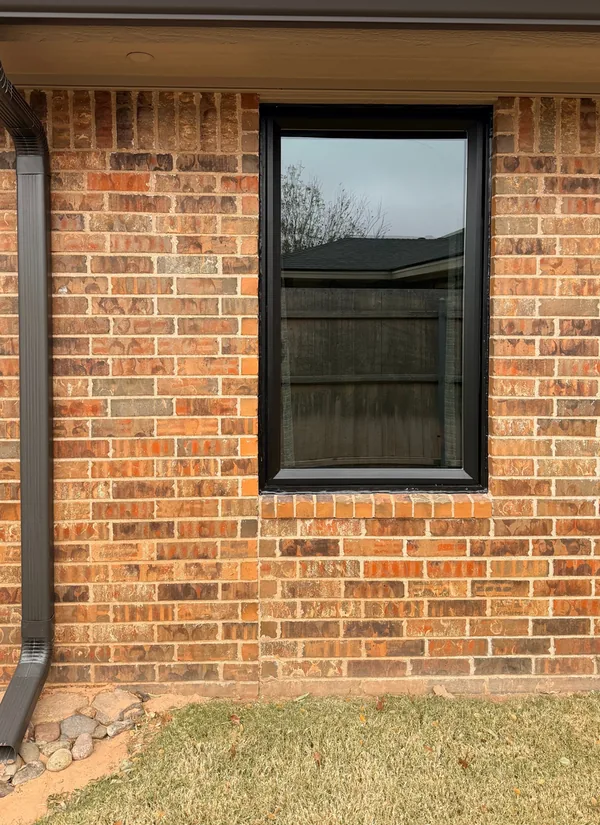 A new black-framed window in a red brick wall, a dark downspout at the corner beside it