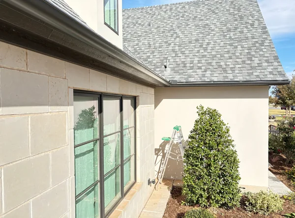 A dark seamless gutter running over black windows on a limestone wall, a ladder at the corner
