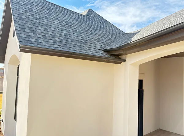 A dark seamless gutter along the roof line of a white stucco home under a grey shingle roof