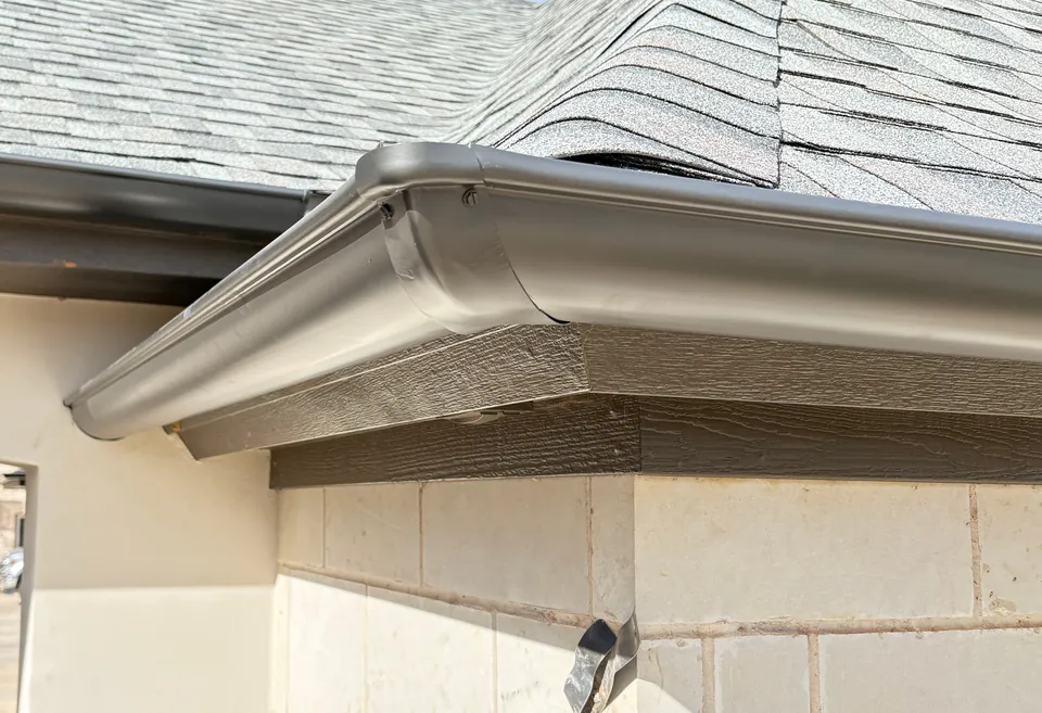 A bronze gutter wrapping a limestone corner under a gray shingle hip roof.