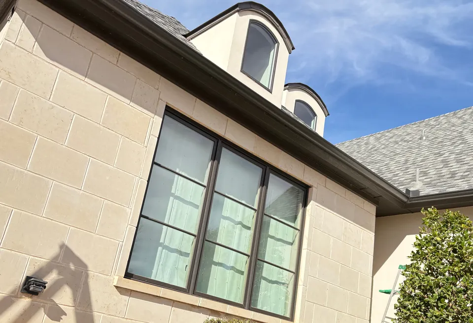 A black-framed window in a limestone wall under two dormers.