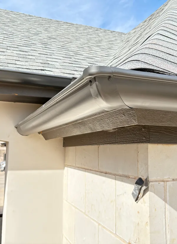 A bronze gutter wrapping a limestone corner under a gray shingle hip roof.
