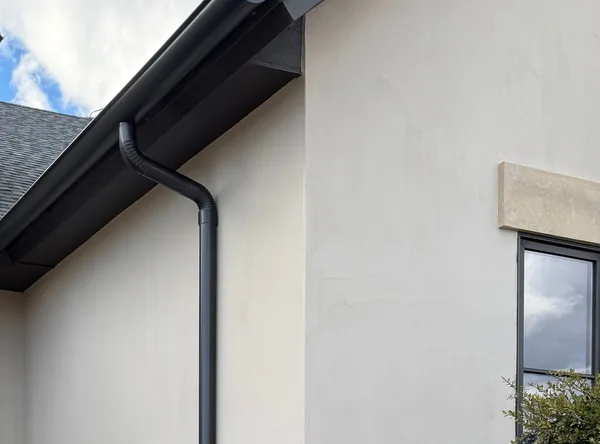 A black seamless gutter and downspout on a white stucco home