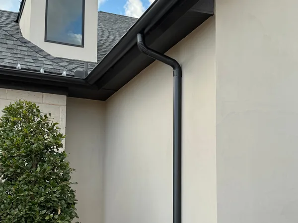 A black gutter and downspout at the corner of a white stucco home under a dormer