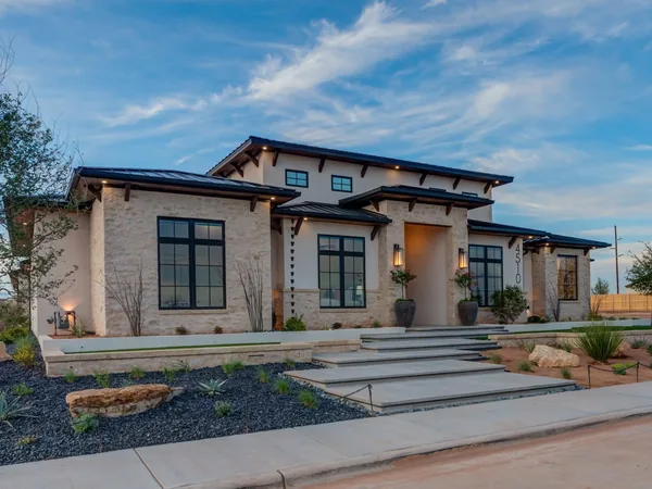 A finished limestone and stucco home with black windows under an evening sky