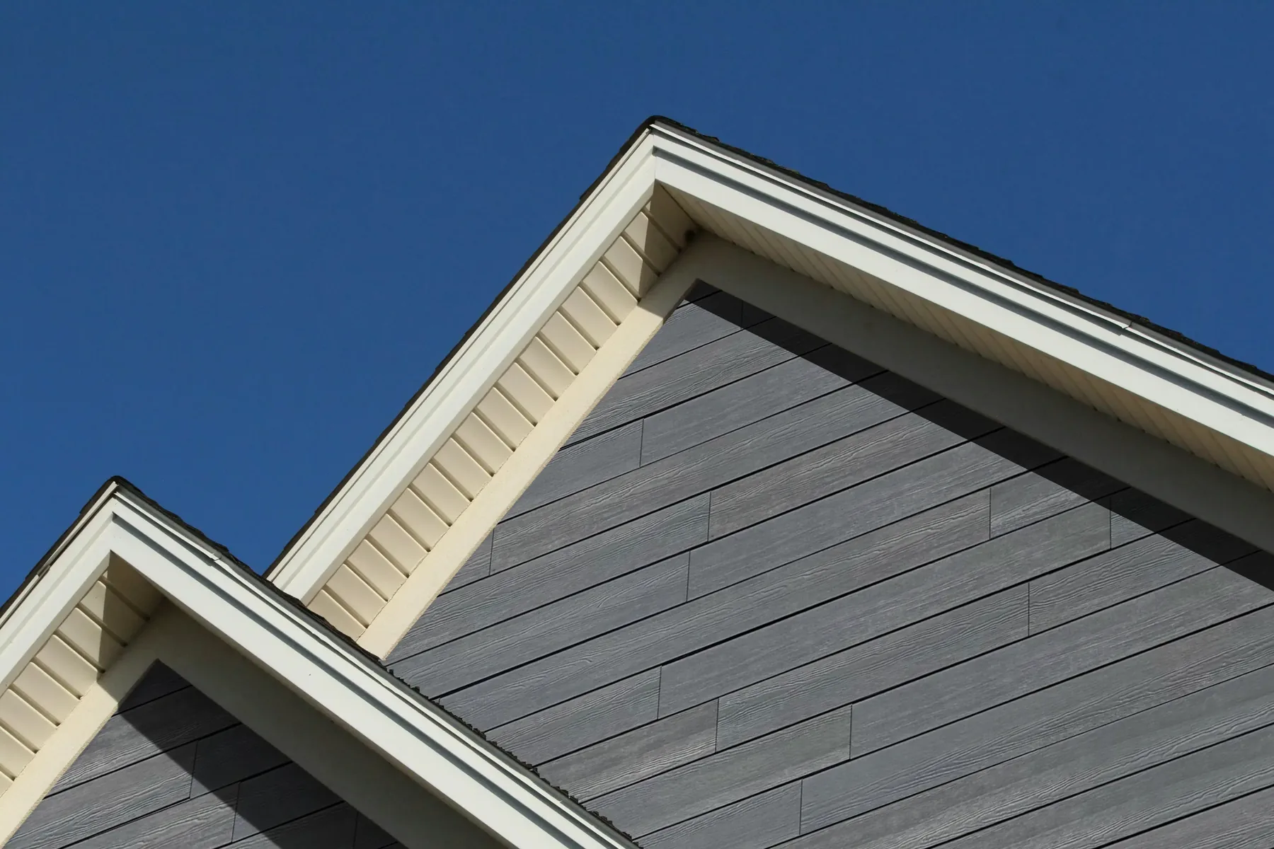 New dark grey lap siding on the gables of a home, with white trim along the roof edges, under a deep blue sky