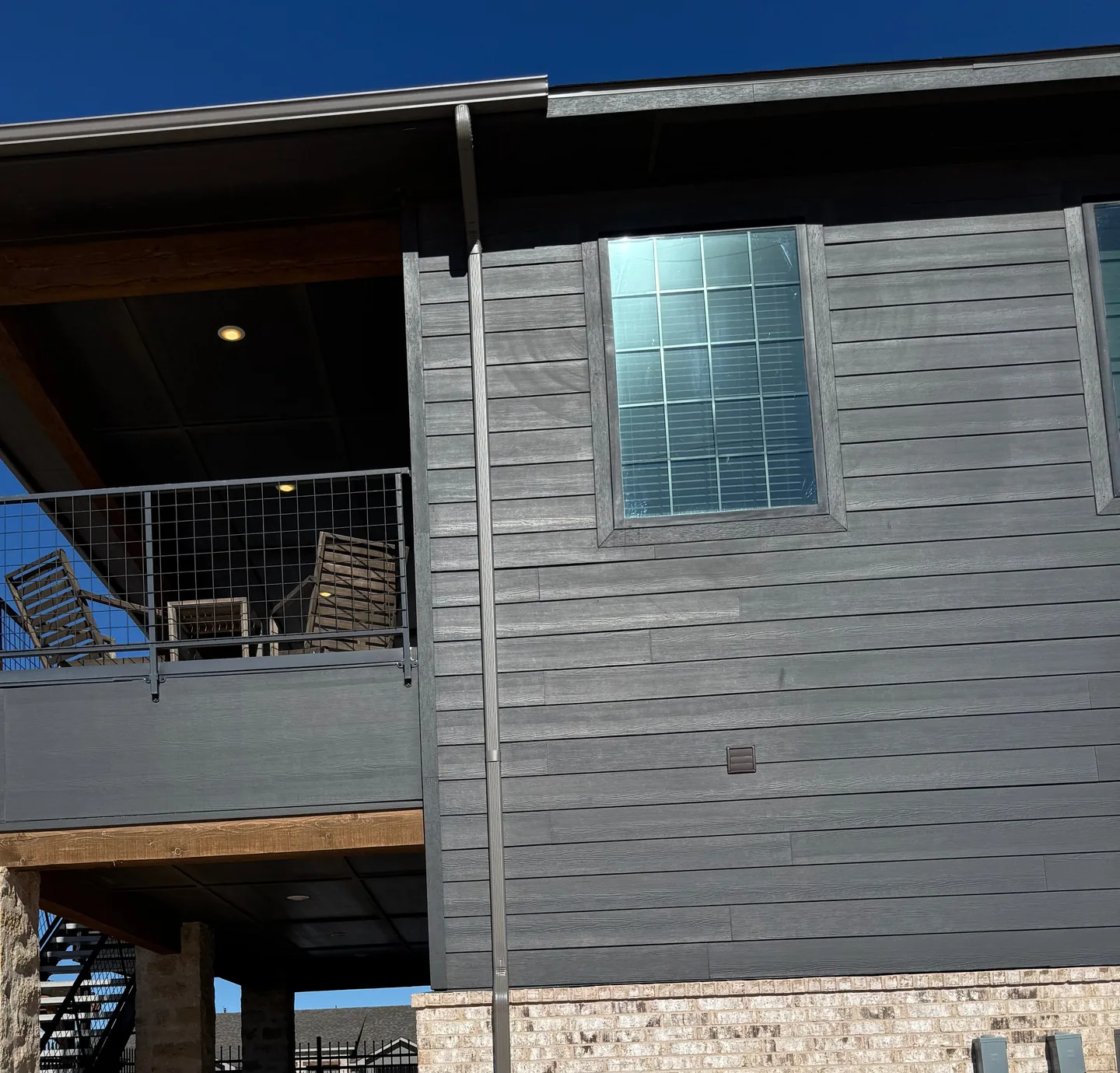 Grey lap siding with a window and a dark gutter and downspout, under a blue sky