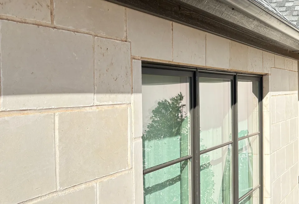 A tall black-framed window in a pale limestone wall, a dark gutter along the roof edge above it.