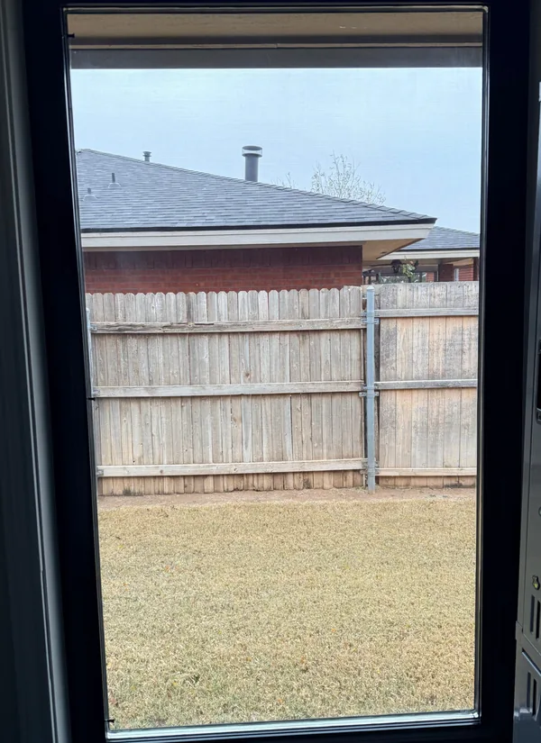 A black-framed window seen from inside, looking out to a lawn, a wood fence and the house next door