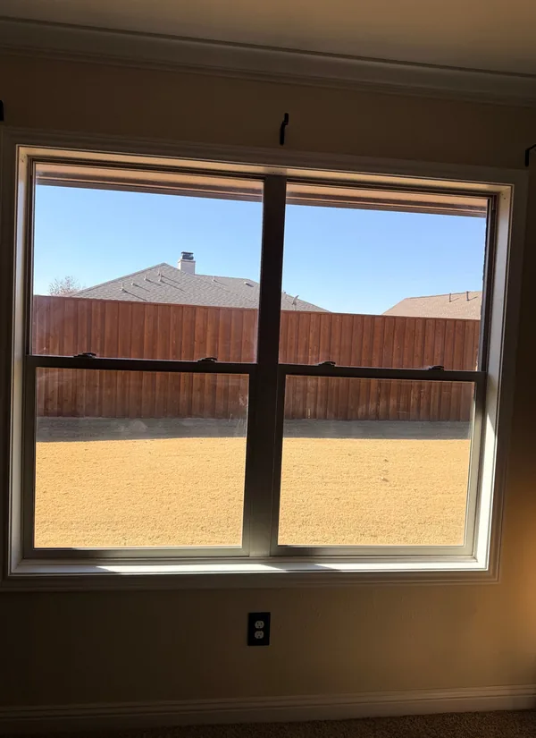 A new double-hung window seen from inside, a wood fence and a blue sky beyond