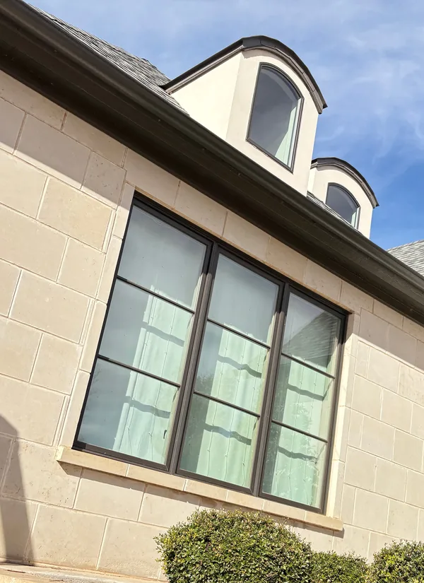 A limestone home with black windows of different sizes under dark gutters
