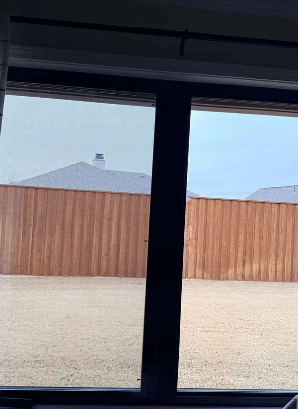 A new black double window seen from inside, a yard and a wood fence beyond