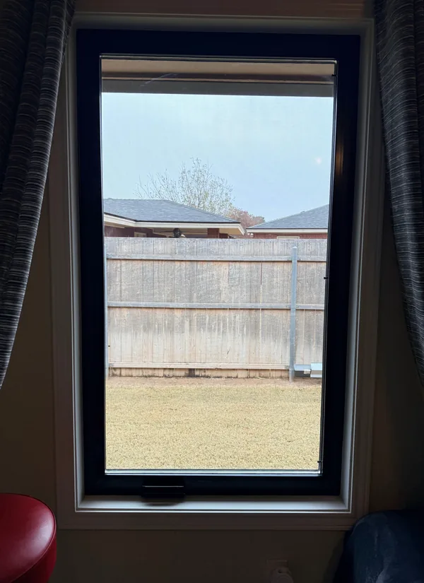 A new black-framed tall window seen from inside, the curtains drawn back, a yard and fence beyond