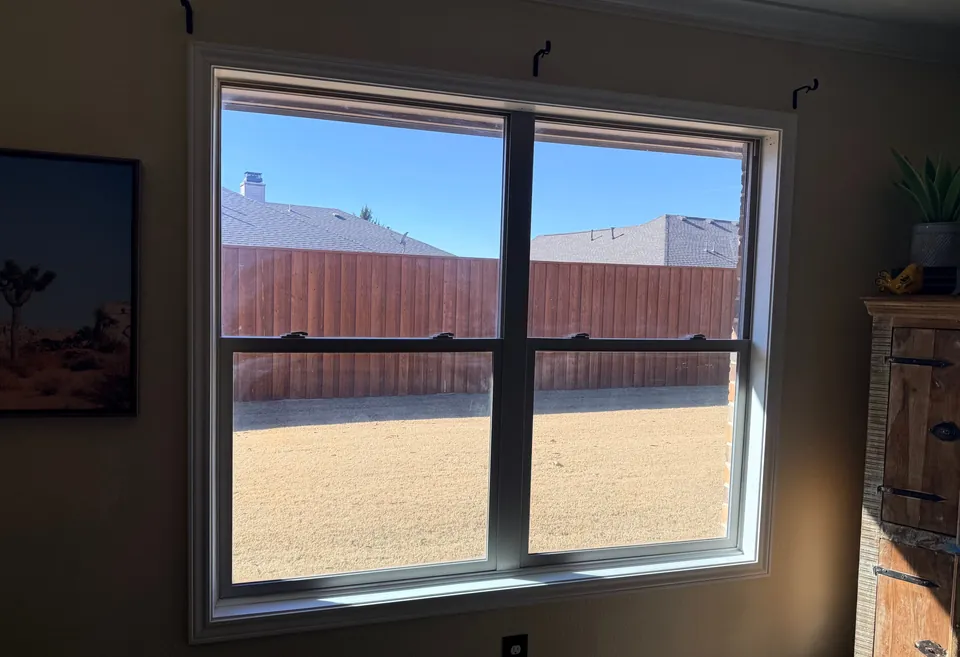 A new double-hung window seen from inside, looking onto a fenced yard under a blue sky.