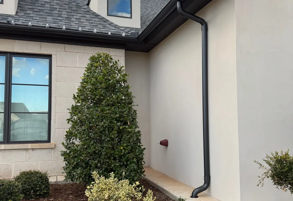 A white stucco home under a dormer, with a black gutter and downspout.